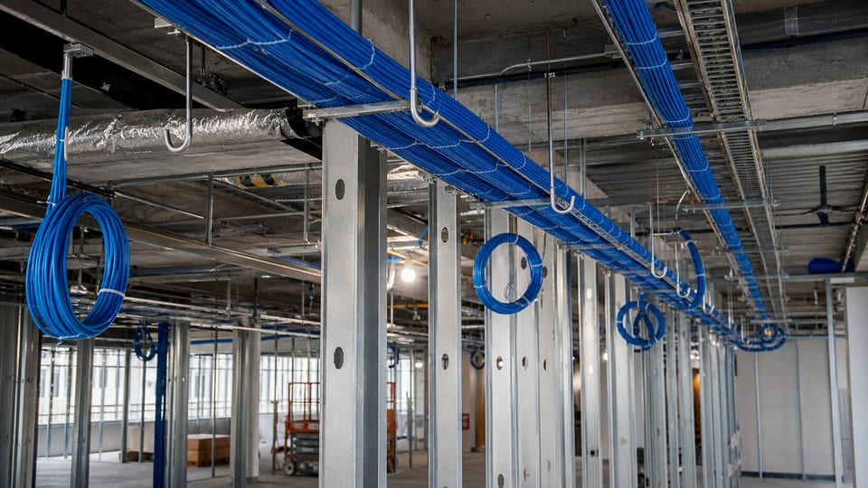 Illustrative commercial renovation with supported blue low-voltage cable pathways above an open ceiling